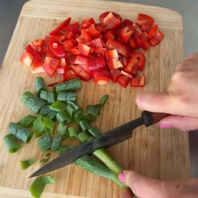 Teriyaki Chicken Drumsticks A person slices green onions on a wooden cutting board with chopped red bell pepper nearby.
