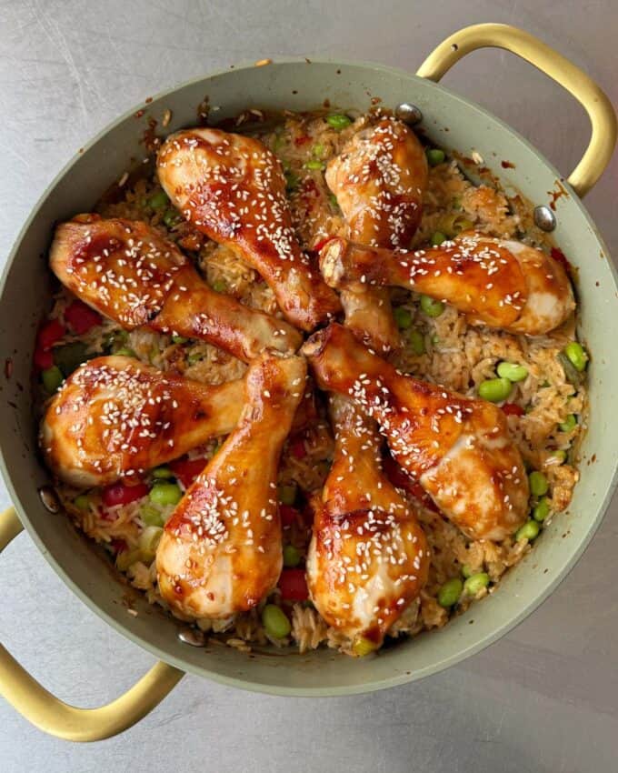 Teriyaki Chicken Drumsticks A pan filled with baked rice, vegetables, and eight glazed chicken drumsticks topped with sesame seeds, arranged in a circular pattern.