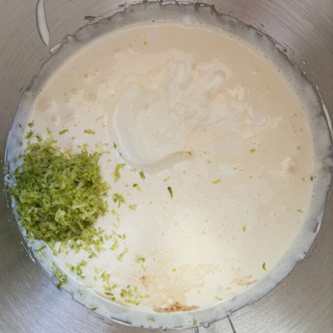 Lime Gingernut Cheesecake A metal bowl containing cream, lime zest, vanilla extract, and sweetened condensed milk, prepared for mixing the Lime Gingernut Cheesecake filling.