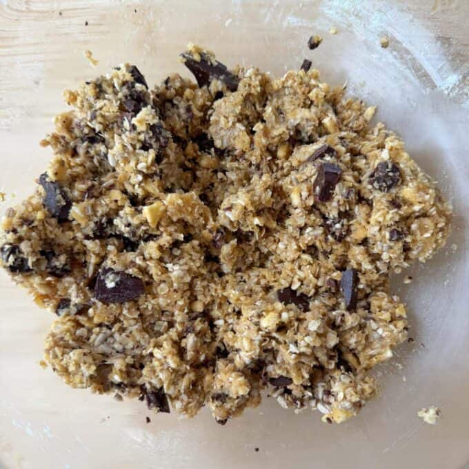 Banana and Dark Chocolate Bumper Bars Unbaked cookie dough mixture with visible oats, chocolate chunks, and nuts in a mixing bowl.