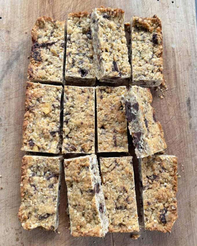Banana and Dark Chocolate Bumper Bars Twelve rectangular oat and chocolate chip bars are arranged on a wooden cutting board.