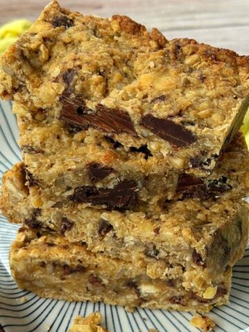 Three thick oat and chocolate chip bars are stacked on a patterned plate, with a yellow cloth in the background.