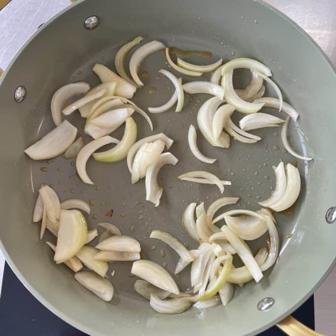 Beef Mince Chow Mein Sliced onions cooking in a frying pan with some oil.