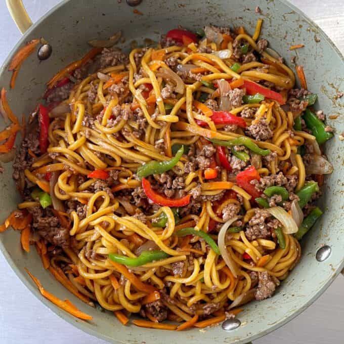 Beef Mince Chow Mein A pan filled with stir-fried noodles, ground meat, sliced bell peppers, carrots, and onions, all mixed together in a savory sauce.