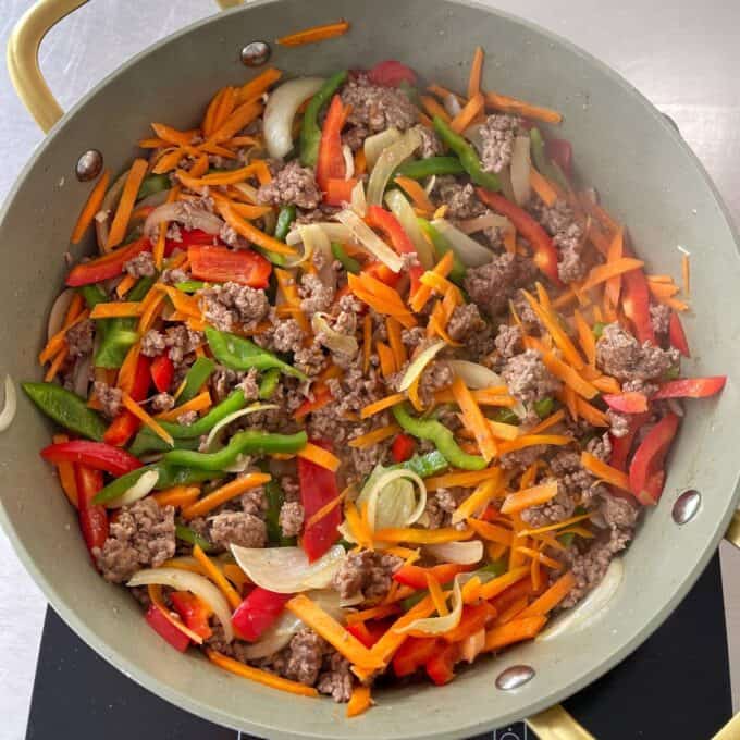 Beef Mince Chow Mein A pan on a stovetop contains ground beef, sliced carrots, bell peppers, and onions being stir-fried.