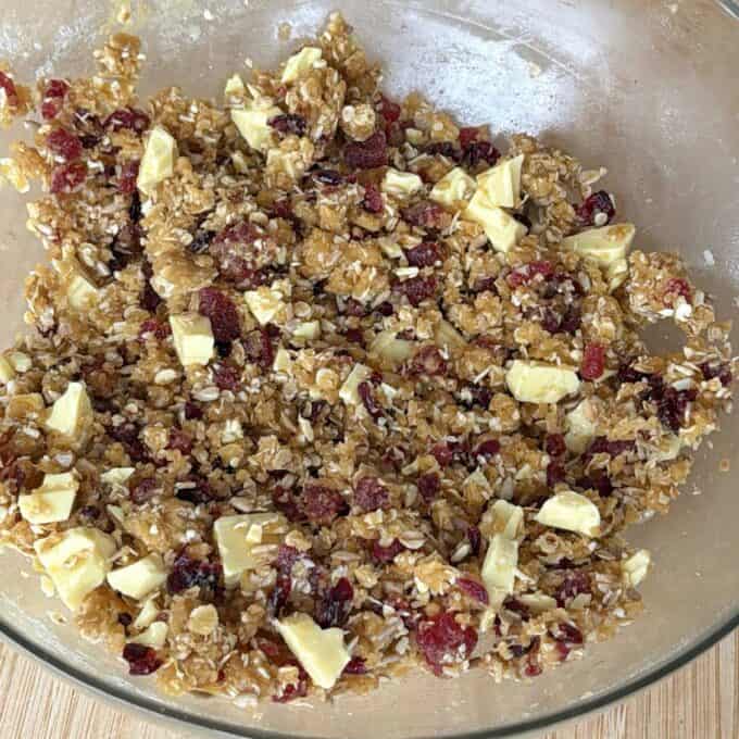 Berry and White Chocolate Bumper Bars A glass bowl filled with a mixture of oats, dried cranberries, white chocolate chunks, and brown sugar, ready for baking.