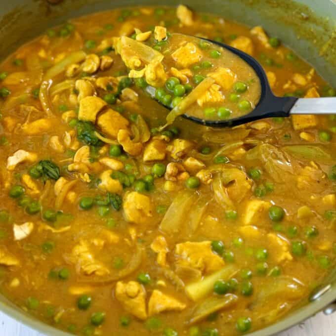 Chicken and Pea Curry A pot of yellow curry with chunks of chicken, green peas, sliced onions, and a ladle scooping up a portion.