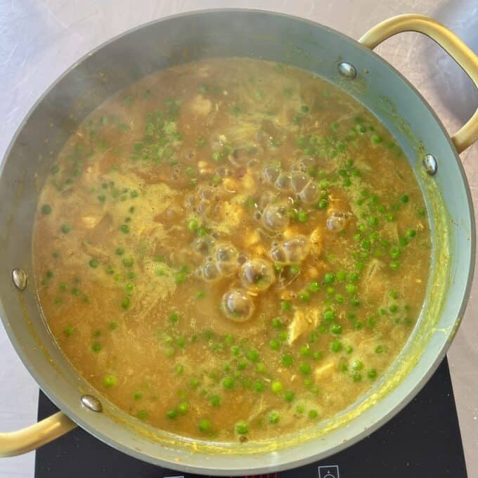 Chicken and Pea Curry A pot of yellow curry with pieces of chicken and green peas simmering on a stovetop.