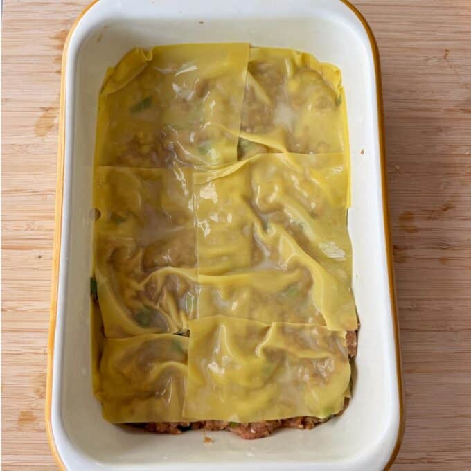 Pork Mince Dumpling Lasagne A baking dish with a layer of uncooked lasagna noodles covering a meat and vegetable mixture.