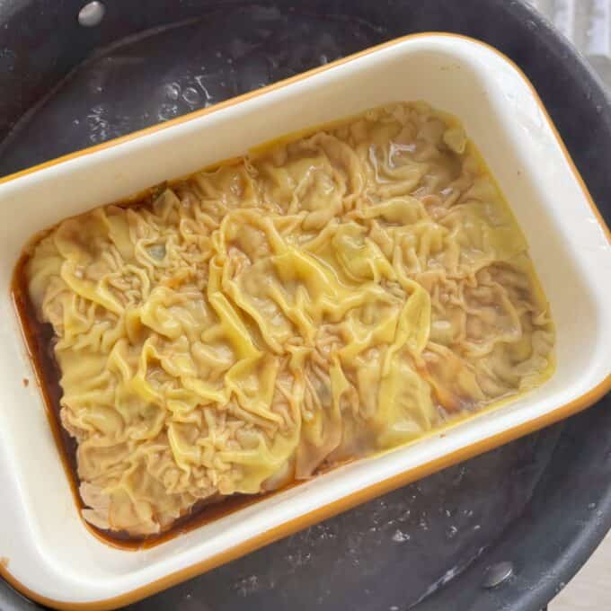 Pork Mince Dumpling Lasagne A rectangular dish filled with dumplings in broth is placed inside a larger pot of boiling water.