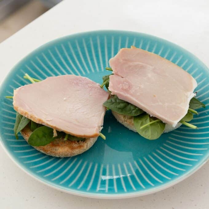 Eggs Benedict with Hollandaise Two halves of an English muffin topped with spinach and slices of ham are arranged on a teal plate.
