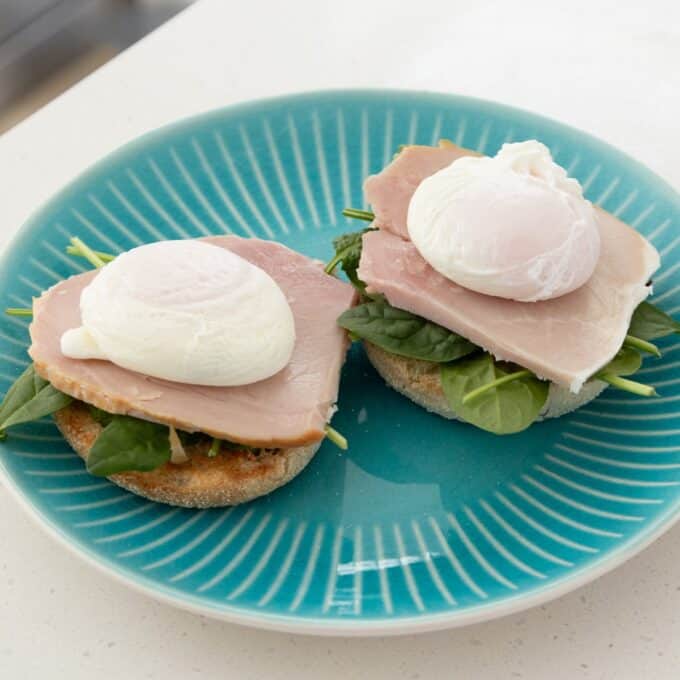 Eggs Benedict with Hollandaise Two halves of an English muffin topped with spinach, sliced turkey, and a poached egg on a turquoise plate.