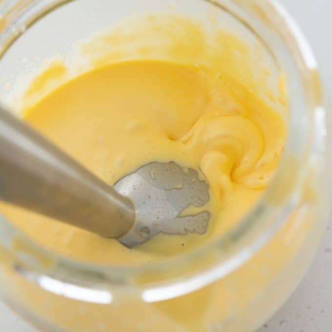 Eggs Benedict with Hollandaise A close-up of a stick blender mixing a thick, yellow, creamy substance in a glass container.