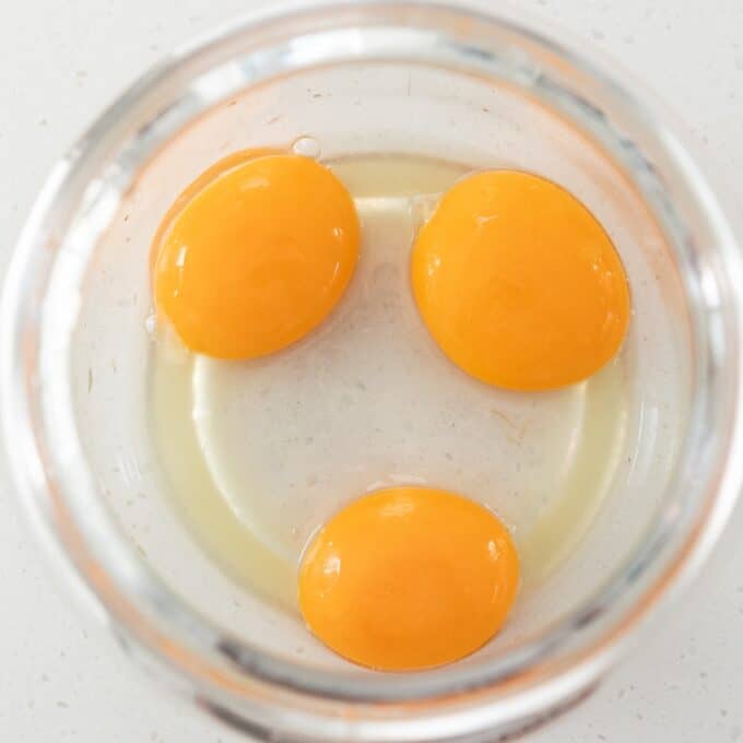 Eggs Benedict with Hollandaise Three raw egg yolks in egg white are in a glass bowl, viewed from above on a white surface.
