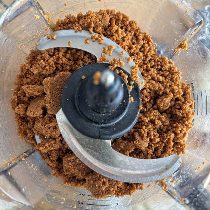 Lime Gingernut Cheesecake Crushed graham crackers processed into fine crumbs inside a food processor.