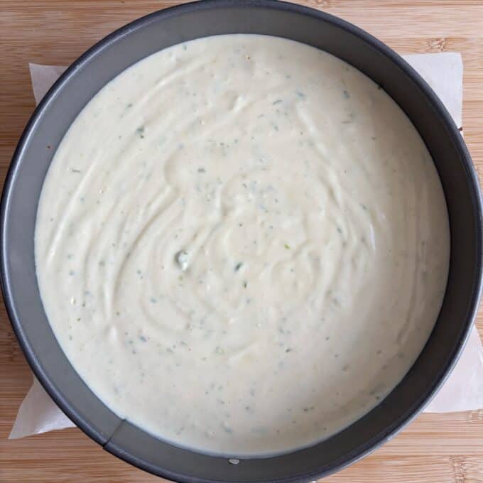 Lime Gingernut Cheesecake A round baking pan filled with an uncooked, smooth, white batter on a wooden surface.