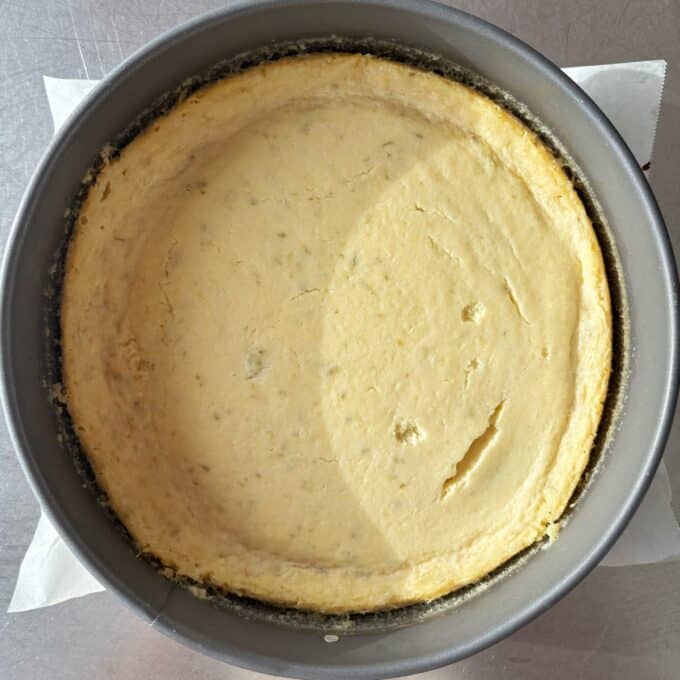 Lime Gingernut Cheesecake A baked cheesecake in a round metal pan, with a slightly uneven surface and a small crack near the edge.