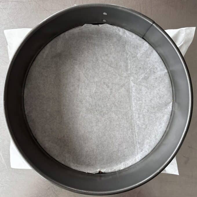 Lime Gingernut Cheesecake A round metal springform cake pan lined with parchment paper on the bottom, placed on a stainless steel surface.
