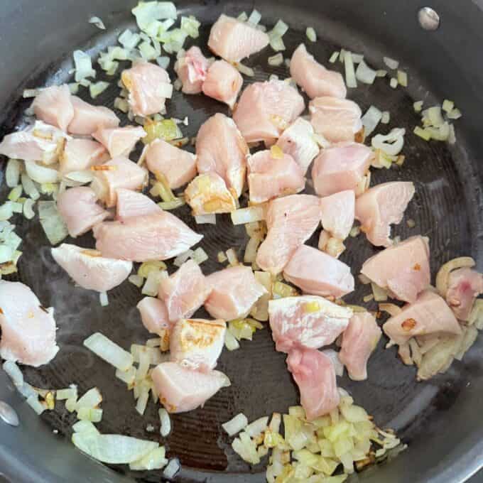 Marry Me Chicken Penne Pasta Diced raw chicken and chopped onions cooking in a frying pan.