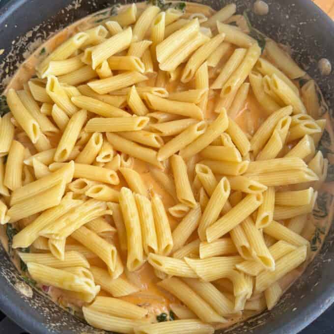 Marry Me Chicken Penne Pasta A skillet filled with penne pasta in a creamy orange sauce with visible spinach or herbs mixed in.