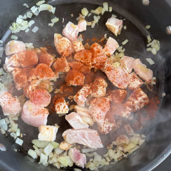Marry Me Chicken Penne Pasta Diced raw chicken, chopped onions, and seasoning cooking in a black skillet. Some steam is visible rising from the pan.