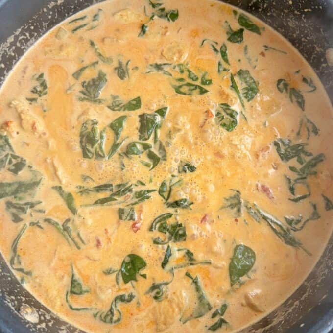 Marry Me Chicken Penne Pasta A close-up of a creamy orange curry simmering in a pot, with visible pieces of spinach and other ingredients mixed in.