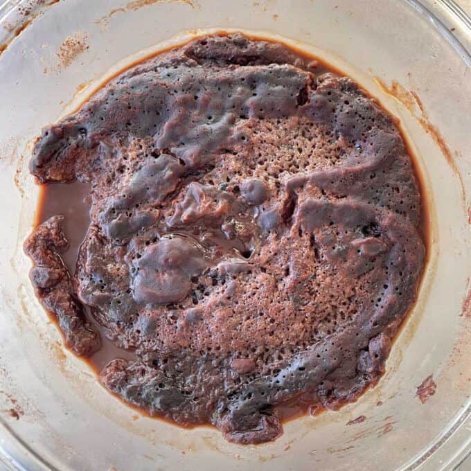 Microwave Self-Saucing Chocolate Pudding A close-up of a chocolate mug cake in a glass bowl, showing a slightly uneven, moist surface with some liquid chocolate around the edges.