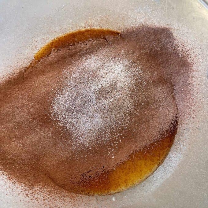 Microwave Self-Saucing Chocolate Pudding A close-up of a glass bowl containing a mixture of ground cinnamon, granulated sugar, and melted butter.