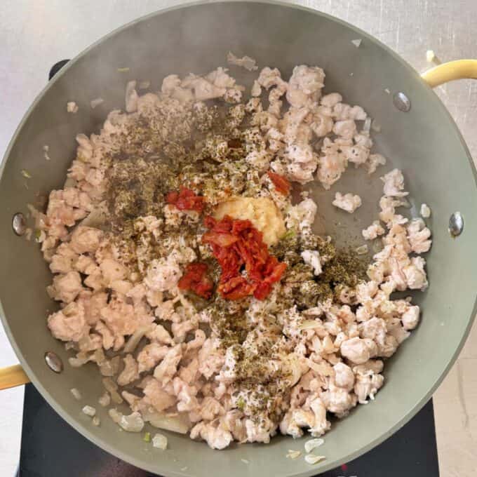 One Pot Creamy Chicken Orzo Ground meat cooking in a skillet with chopped onions, tomato paste, minced garlic, and dried herbs added on top.