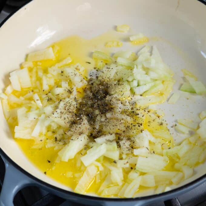 Shepherd's Pie Chopped onions with dried herbs and oil in a white pan on a stovetop, beginning to sauté.