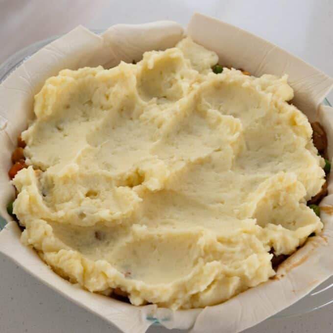 Shepherd's Pie A pie dish lined with parchment paper containing a layer of mashed potatoes spread over a vegetable filling, prepared for baking.