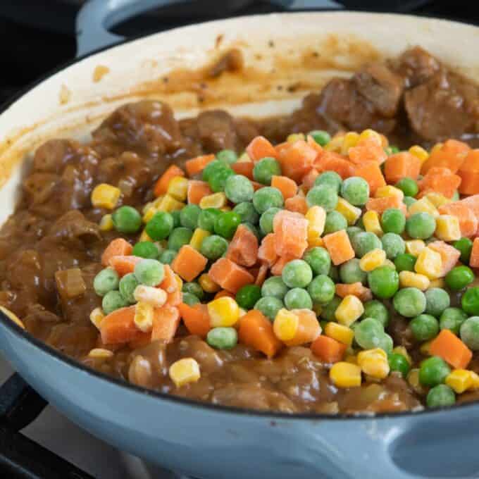 Shepherd's Pie A pot of stew with chunks of meat and brown gravy, topped with a pile of frozen mixed vegetables including peas, carrots, and corn.