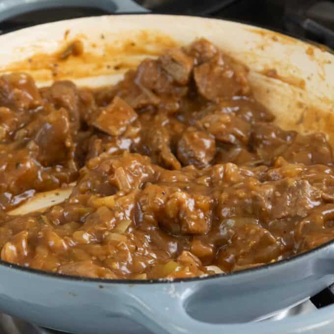 Shepherd's Pie Chunks of beef in a thick brown gravy simmering in a light blue Dutch oven on a stovetop.