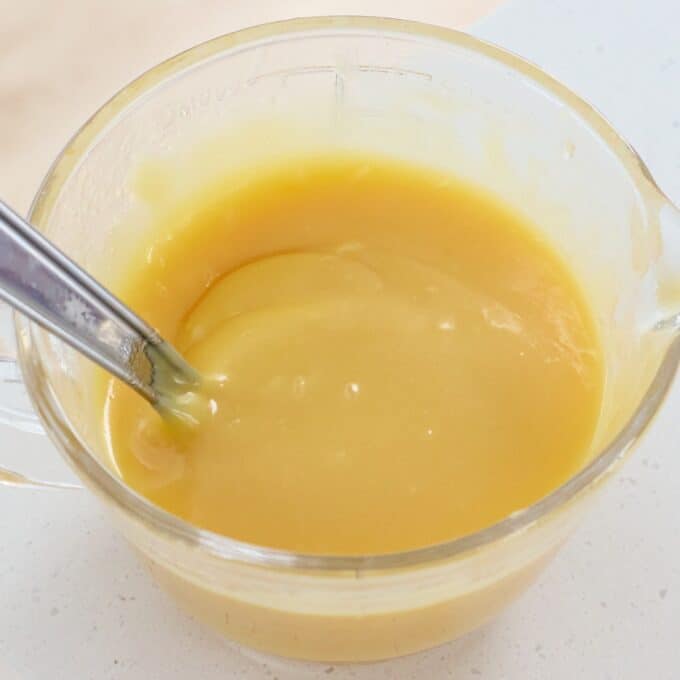 Sprinkle Biscuit Slice A glass measuring cup filled with yellow lemon curd, with a metal spoon resting inside.