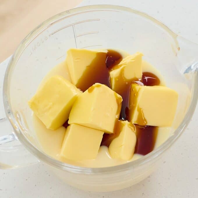 Sprinkle Biscuit Slice Cubed butter, sweetened condensed milk, and dark liquid (likely vanilla extract or syrup) in a glass measuring cup.