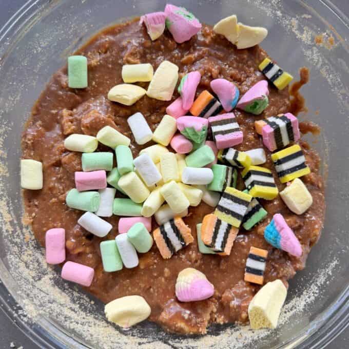 XL Pick and Mix Lolly Slice A glass bowl filled with brown batter, topped with colorful mini marshmallows and pieces of licorice allsorts candy.