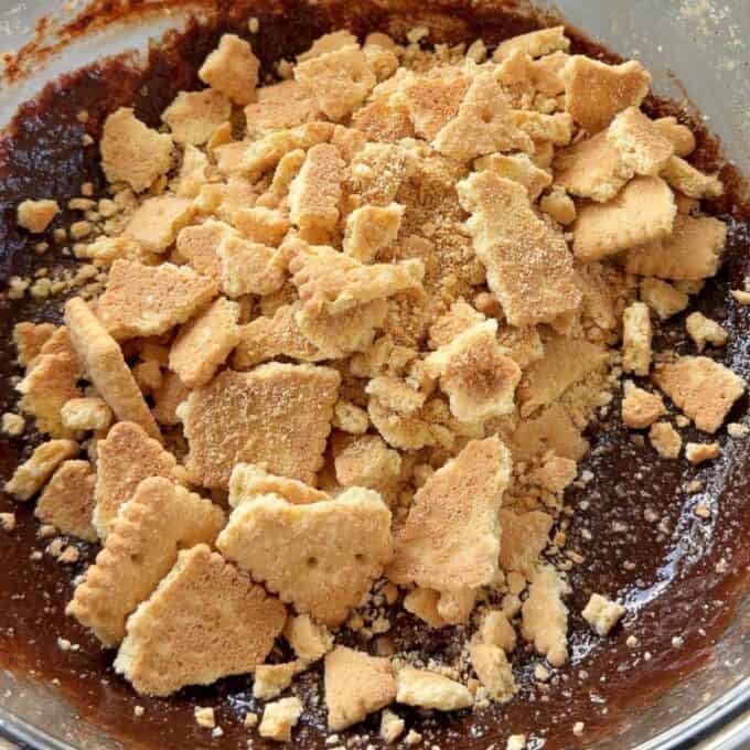 Love Heart Lolly Slice Crushed biscuits are scattered on top of a bowl of chocolate batter, ready to be mixed together.