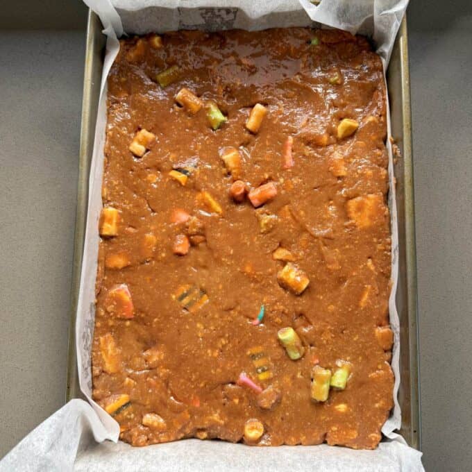 XL Pick and Mix Lolly Slice A rectangular baking tray lined with parchment paper is filled with unbaked brown batter containing colorful candy pieces.