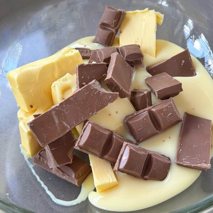 XL Pick and Mix Lolly Slice A glass bowl containing chunks of milk chocolate, blocks of butter, and a pool of sweetened condensed milk.