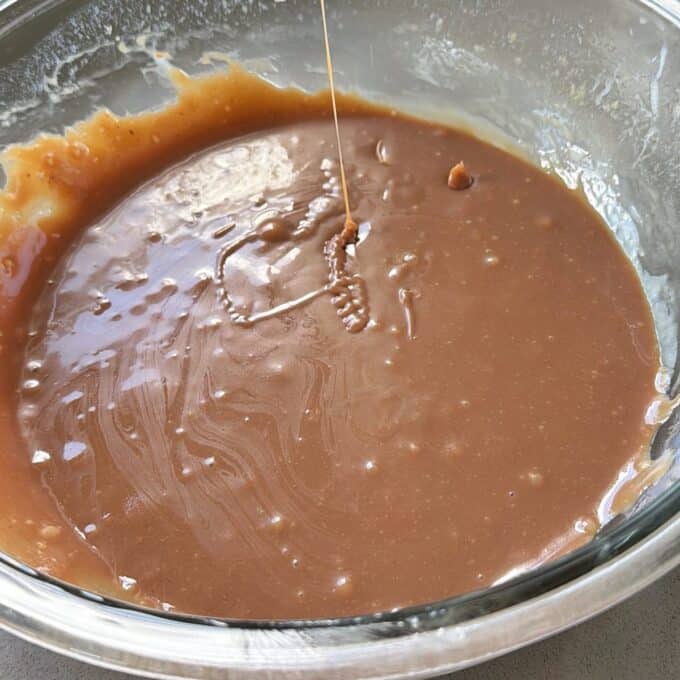 XL Pick and Mix Lolly Slice A glass bowl filled with smooth, light brown caramel sauce or batter, with a thin stream dripping into the mixture.