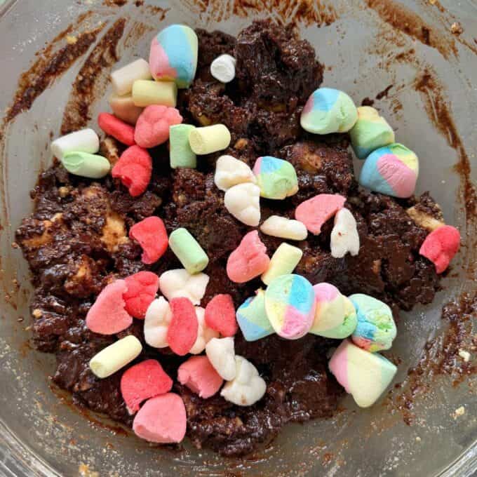 Love Heart Lolly Slice A glass bowl filled with chocolate mixture, crumbled cookies, and colorful mini marshmallows.