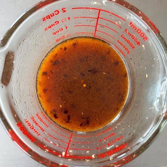 Zesty Tuna, Avocado and Edamame Salad A glass measuring cup filled with a reddish-brown liquid marinade, viewed from above, on a stainless steel surface.