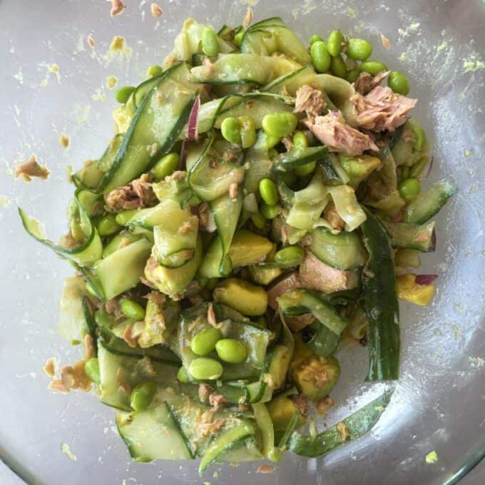 Zesty Tuna, Avocado and Edamame Salad Salad with sliced cucumber, edamame, tuna chunks, red onion, and avocado, mixed in a clear bowl.