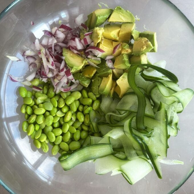 Zesty Tuna, Avocado and Edamame Salad A glass bowl containing chopped red onion, diced avocado, shelled edamame, and ribboned cucumber, arranged in separate sections.