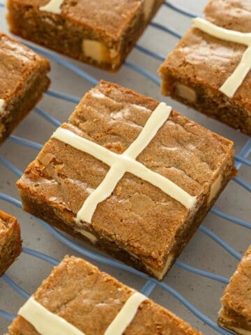 Square Hot Cross Blondie bars with white icing crosses on top, arranged neatly on a blue wire cooling rack.