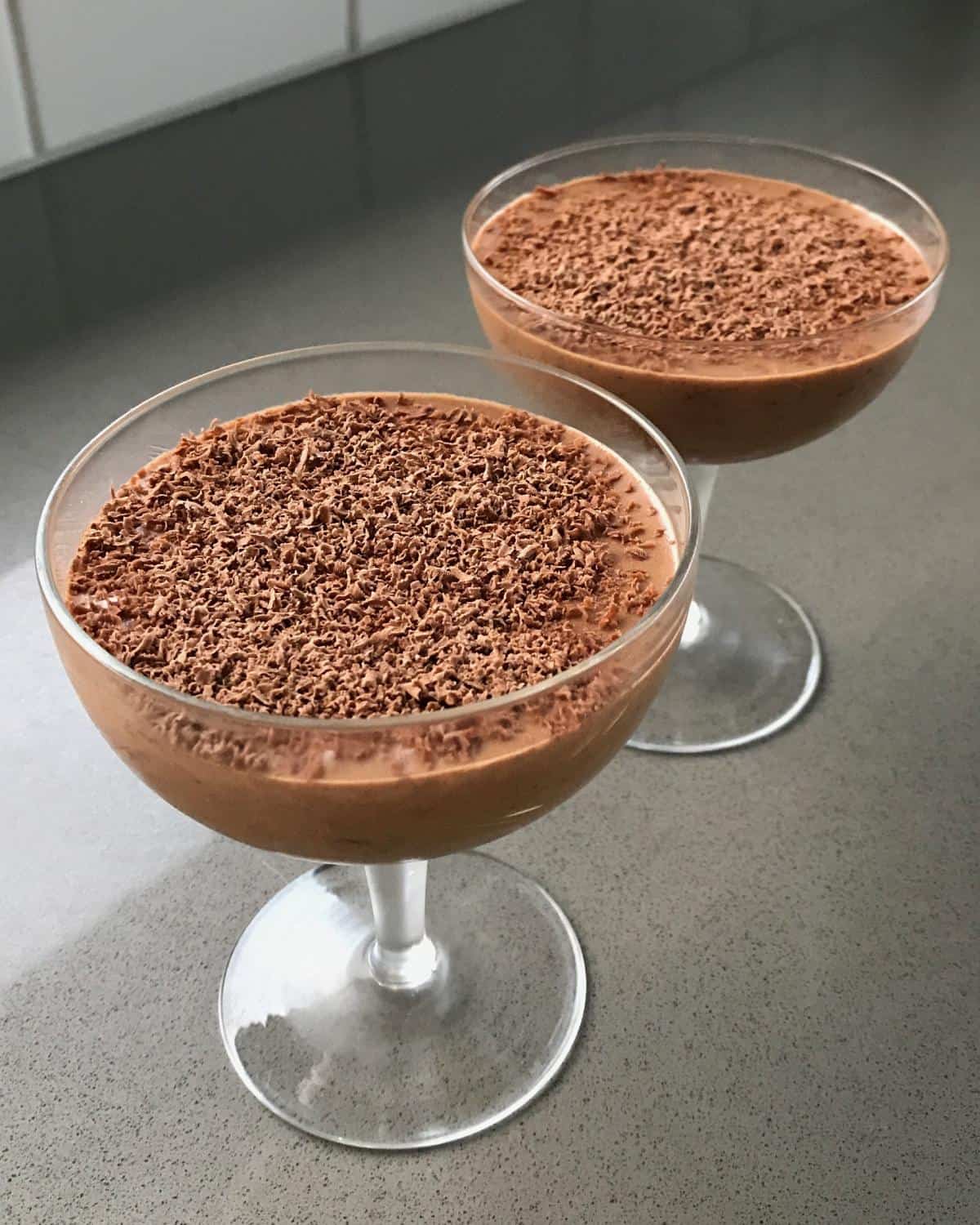 Simple Chocolate Mousse Two glass dessert cups filled with chocolate mousse, topped with grated chocolate, placed on a gray countertop.