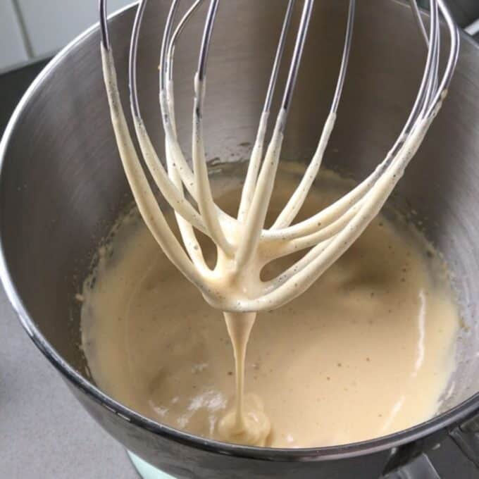 Simple Chocolate Mousse A metal whisk attachment with pale batter dripping off is lifted above a mixing bowl, with more batter inside the bowl.
