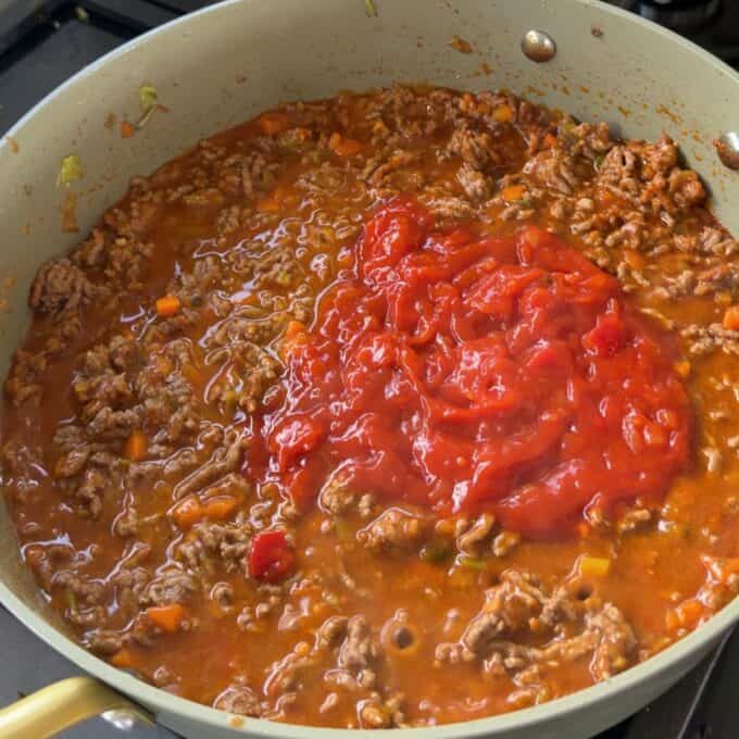 Cheesy Taco Mince and Macaroni Bake A skillet filled with ground meat, tomato sauce, and vegetables cooking on a stovetop.