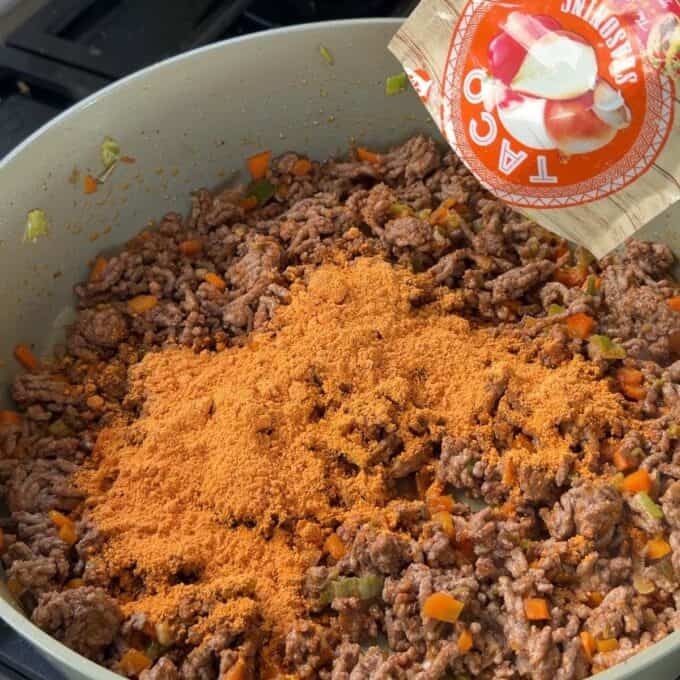 Cheesy Taco Mince and Macaroni Bake Ground beef, diced vegetables, and a packet of taco seasoning are being cooked together in a pan.