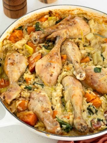 Baked chicken drumsticks on a bed of creamy rice with vegetables in a white baking dish.